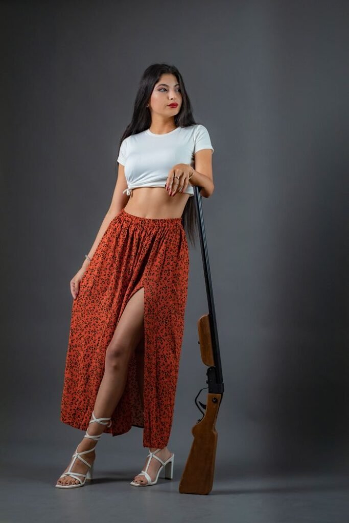 Fashionable woman in elegant attire posing confidently indoors with a rifle.